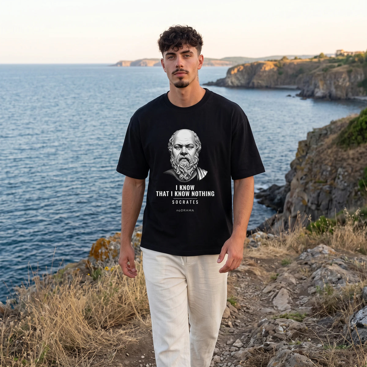 Мъж с черна oversized тениска Сократ на скалите над морето noDRAMA